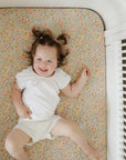 Baby smiles on mushie Extra Soft Muslin Crib Sheet in white crib with floral mattress.