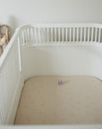 White crib with mushie Extra Soft Muslin Crib Sheet, purple pacifier, and stacked toy rings.