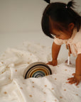 A toddler plays with stacking bowls on a mushie Organic Cotton Muslin Swaddle Blanket.