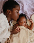 A child kisses a baby wrapped in a towel, their skin soft with mushie Baby Cream.