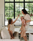 A girl enjoys mushie Kaleidoscopes while a mom with a baby smiles in a bright living room.
