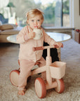 Toddler on a pink tricycle sipping from a Mushie Bluey x Mushie Silicone Training Cup + Straw.