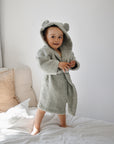 Toddlers stand on a bed wearing the mushie Bear Robe with hood and ears.