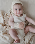 Smiling baby on mushie Organic Cotton Muslin Swaddle Blanket, wearing a teething mitten.