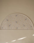The Bluey x Mushie Silicone Placemat by mushie is semicircular, white, and features multicolored stars, hearts, and cute cartoon animals on a light background. The word "mushie" is embossed in the bottom corner for a charming kids’ placemat.
