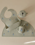 Mushie Bluey x Mushie Silicone Baby Bib in sage green, featuring Bluey characters, neatly displayed on a light background with matching placemat, sippy cup, and snack cup.