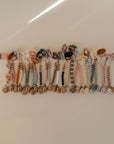 A row of mushie Silicone Pacifier Clips | Mila, featuring food-grade silicone and natural wood accents, arranged neatly on a light surface. The clips are shown in a variety of pastel and neutral shades.