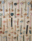 The mushie Linen Pacifier Clip 2-Pack features pastel wooden clasps in animal and flower shapes, colorful silicone beads, and linen clips—perfect for hanging pacifiers neatly on any wall.
