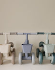 Three mushie Mini Toddler Bikes in beige, blue-grey, and sage green, each with a front basket.