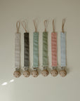 Two mushie linen pacifier clips with wooden clasps displayed on a light surface.