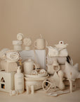 A neatly arranged display of mushie's Star Lovey Blanket with coordinating neutral baby toys, bottles, pacifiers, bibs, washcloths, pillow, stacked towels, and lotion—all set against a beige background.