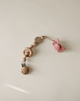 The mushie Silicone Pacifier Clip | Mila features natural wood beads and a pink butterfly-shaped silicone pacifier, shown resting on a light beige surface.