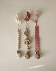 Three mushie pacifiers are displayed with unique clips: a Silicone Pacifier Clip | Mila, a natural wood clip, and a pink fabric clip. Each features butterfly-shaped or simple food-grade silicone designs on a neutral background.