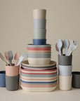 A neatly arranged set of mushie Square Dinnerware Plates, BPA-free and pastel-colored, stacked and grouped in an organized manner against a neutral background.
