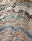 A stack of patterned, water-resistant mushie Long Sleeve Bibs with floral and checkered designs.