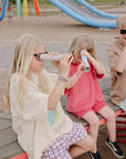 Three kids on a bench enjoy play with mushie Kaleidoscopes.