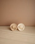 The FRIGG Rope Silicone Pacifier 2-Pack | Limited Edition by FRIGG features two beige silicone pacifiers with round handles and textured edges—perfect essentials for soothing your baby in style.
