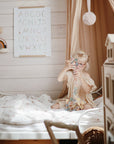 Girl plays on bed with mushie HEX Connect Building Toy Set in cozy, softly lit bedroom.