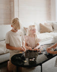 Three kids play with the mushie HEX Connect Building Toy Set on a black coffee table.