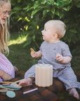 Two children sitting on a blanket outdoors with the mushie Coin and Tube Sorting toy.
