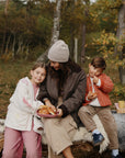 A woman and two children sit on a log, sharing pastries from a mushie Square Dinnerware Plate.