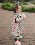 Toddler wears mushie Linen Pacifier Clip 2-Pack while drinking outdoors in a heart-print outfit.