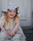 Young girl in a floral dress and hat holds a mushie Silicone Sensory Toy.