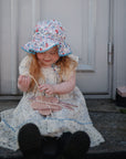 Young girl in a floral dress plays with a mushie Silicone Sensory Toy on the doorstep.