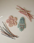 Mushie Silicone Sensory Toy: pink flower & blue rocket for fine motor play on light surfaces.