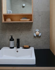 A modern bathroom sink with towels, toiletries, and a soap dispenser sits by a gray tile wall. The mushie Suction Spinner Toy adds playful sensory fun next to the sink.