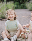 Two toddlers smile on a path with flowers, enjoying the mushie Bluey Gift Set essentials.