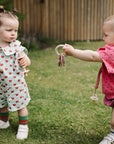 Two toddlers on grass, one gives a mushie Teething Ring to the other.