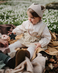 Baby with a crown headband uses FRIGG Daisy Natural Rubber Pacifier while playing on a blanket.