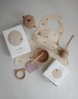 Flat lay of mushie baby feeding and teething essentials, featuring a rainbow bib, bowl, spoon, teether, sippy cup, rattle, and the mushie Silicone Placemat—all designed for safe mealtimes.