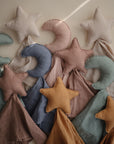 Mushie’s Star Lovey Blanket features soft plush star toys in cream, blush pink, light blue, sage green, and mustard yellow, each attached to a matching organic cotton blanket and styled on a neutral background.