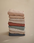 A neatly folded stack of mushie Extra Soft Muslin Changing Pad Covers in assorted pastel solids, stripes, and dots rests on a neutral beige surface.
