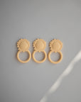 Three mushie Lion Teether toys in beige, shaped like cute lion faces, are lined up on a light gray surface with a gentle shadow. These non-toxic teethers provide safe, soothing relief for teething babies.