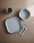 The mushie Square Dinnerware Plates set features BPA-free silicone dishware in light gray, including a plate, bowl, cup, fork, and spoon—an ideal alternative to plastic dinnerware for children.