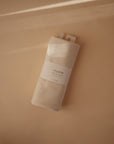 The Mushie Ribbed Baby Blanket in beige, made from organic cotton, is neatly rolled with a white label and displayed on a soft beige background under natural light with gentle shadows.