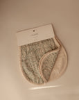 A partially folded mushie Organic Cotton Muslin Burp Cloth from the 2-Pack set is shown under a white branded label on a neutral background, featuring a paisley pattern and beige trim.