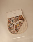 The mushie Organic Cotton Muslin Burp Cloth 2-Pack, featuring a colorful floral-patterned baby bib with a cream lining and soft cotton burp cloths, is shown with branded packaging on a beige background.