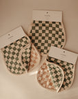 Two organic cotton muslin burp cloths by mushie, in green and beige checkered patterns with white borders, are shown on a neutral background. Packaging displays the mushie brand.