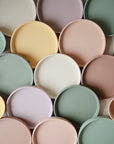 The Mushie Classic Silicone Suction Plates, in pastel yellow, pink, green, lavender, and cream, are non-toxic and closely arranged for a colorful display—perfect for safe toddler mealtimes.