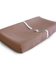 The mushie Extra Soft Muslin Changing Pad Cover in brown features two white safety straps and is shown on a white background.