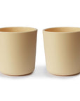 Two identical mushie Dinnerware Cups in beige are placed side by side on a white background, offering a non-toxic and stylish solution for kids' everyday use.