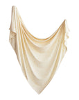 The mushie Stretchy Swaddle in cream, featuring a subtle pattern of small yellow dots, is elegantly draped on a white background with gentle folds forming a neat triangle shape.