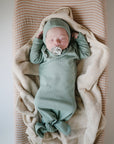 A newborn sleeps peacefully with a pacifier, dressed in soft green, on a striped cushion topped with the mushie Extra Soft Muslin Changing Pad Cover.