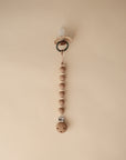 The mushie Silicone Pacifier Clip | Luna in beige features food-grade silicone and wooden beads, displayed vertically on a plain light tan background.