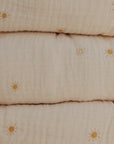 The mushie Extra Soft Muslin Changing Pad Cover features a crinkled beige muslin fabric with a subtle pattern of small yellow sun illustrations scattered across the surface.