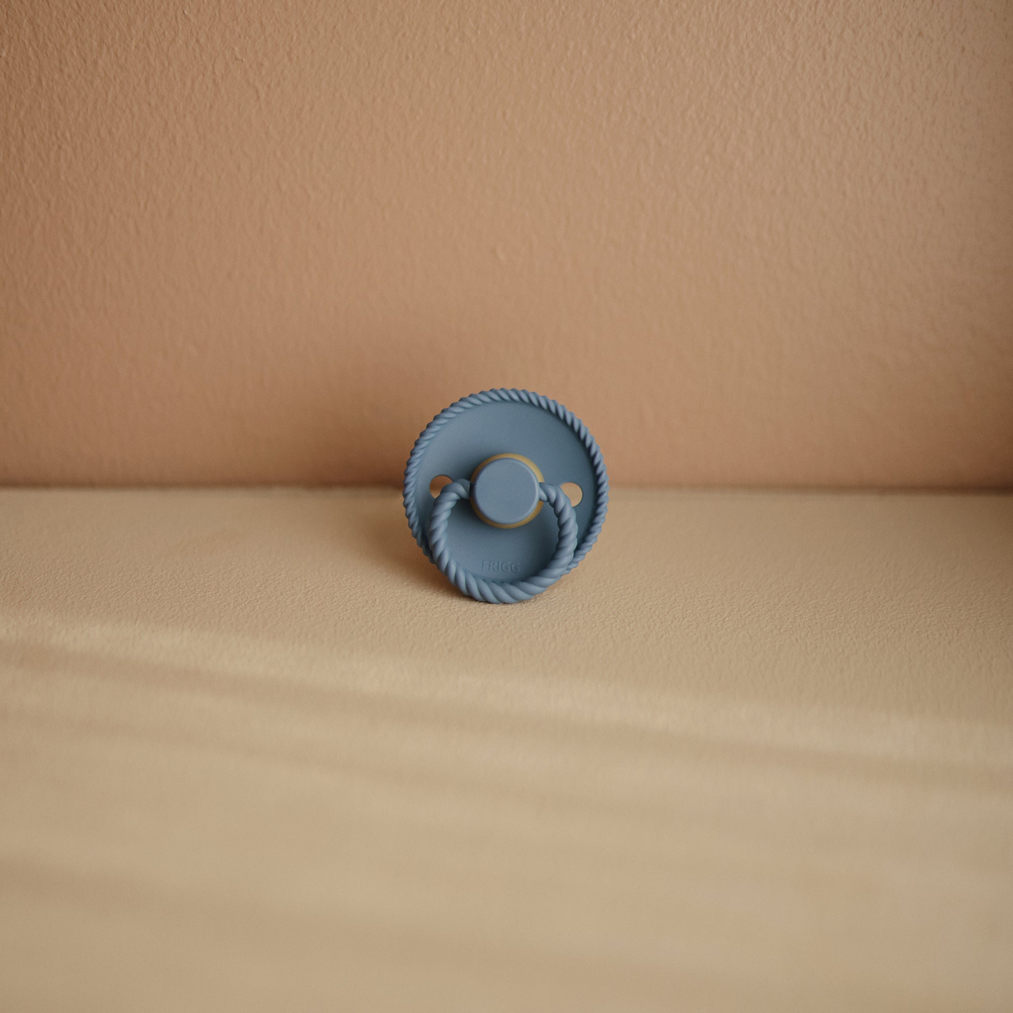 Frigg Moon Rubber Ocean View pacifier on a beige surface. 